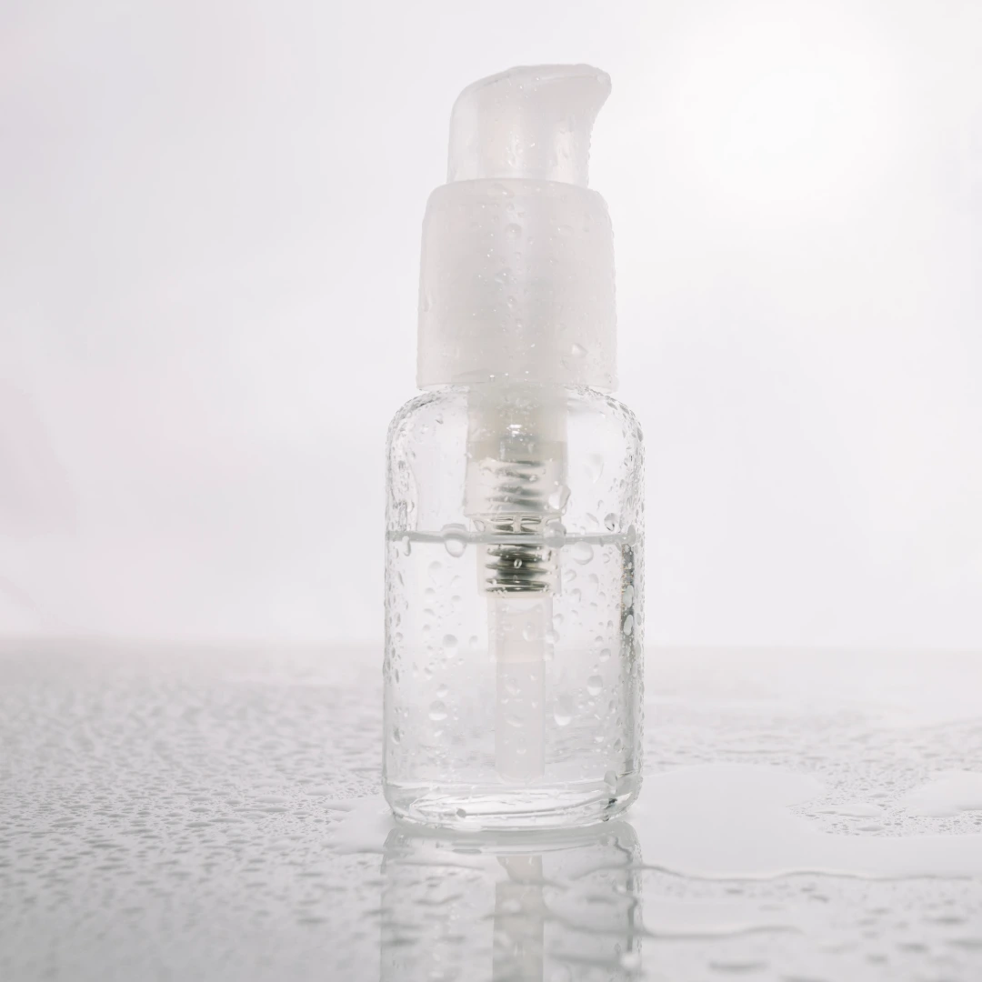 Minimalistisches, cremeweißes Kosmetik-Arrangement mit einer Serumflasche, einem Schälchen mit Gesichtsöl und einem Pinsel für eine salicylsäurefreie Hautpflege bei der Guaifenesin-Therapie