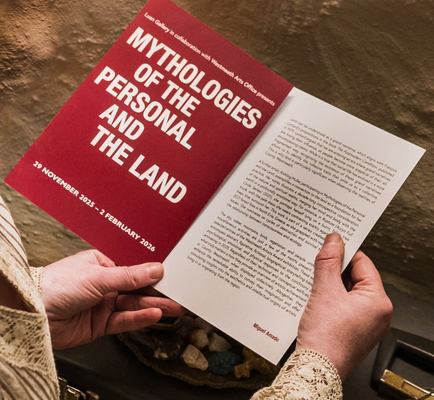A person holds a red publication titled Mythologies of the Personal and the Land.