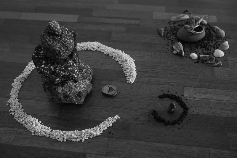 An upright volcanic rock is surrounded by a crescent of white fragments, with a smaller spiral arrangement beside it.