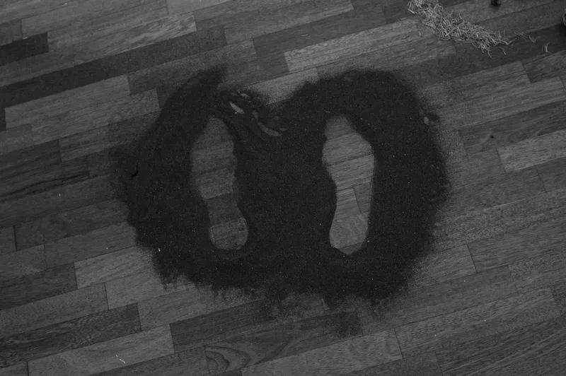 Two footprint-shaped openings are formed within a dark mass of organic material arranged on a wooden floor.