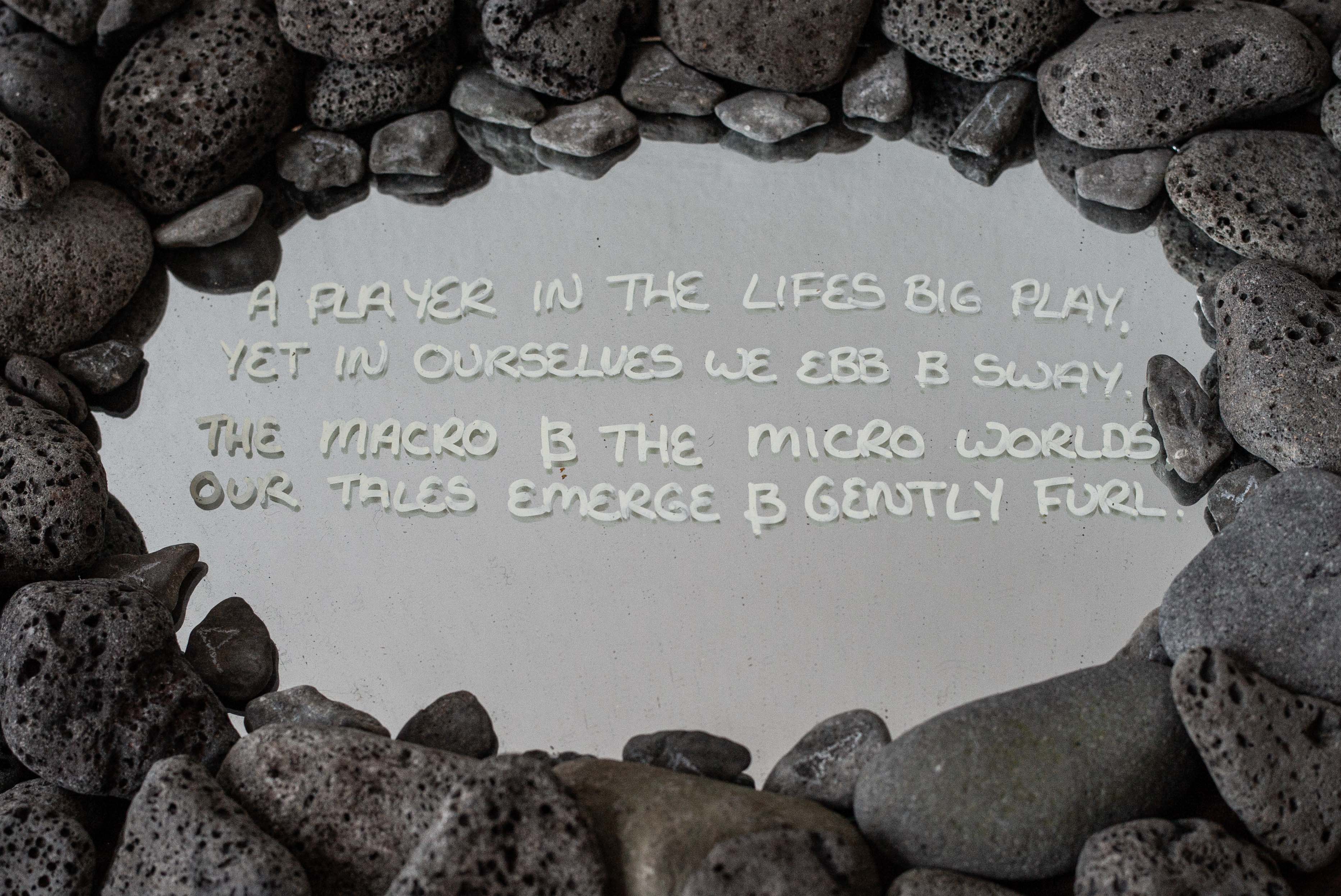 A handwritten participatory message displayed on a pale surface and surrounded by a circle of dark volcanic stones.