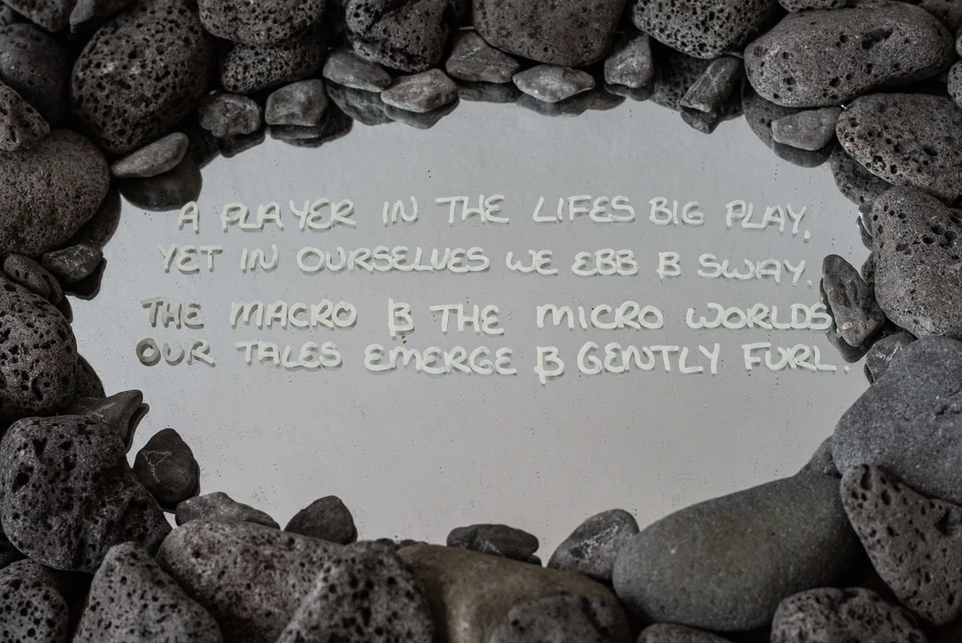 A handwritten participatory message displayed on a pale surface and surrounded by a circle of dark volcanic stones.