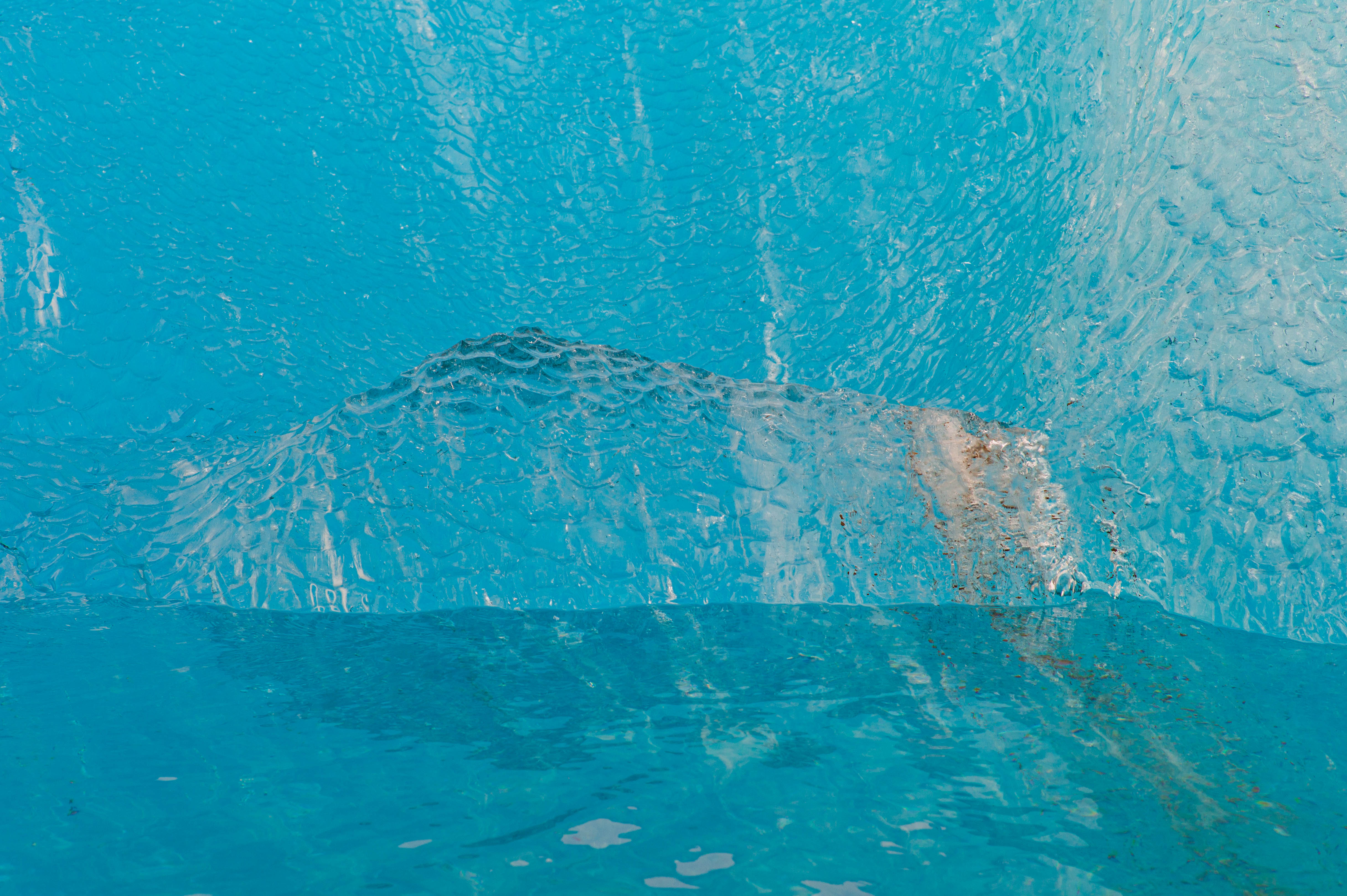 Close view of translucent blue ice containing fine cracks, suspended sediment and shifting patterns of light.
