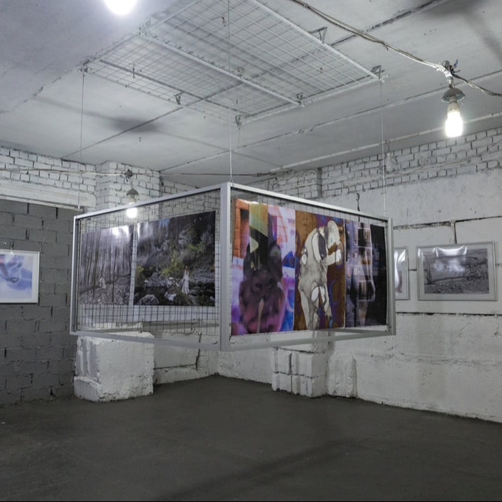 Gallery installation of photographic works suspended from translucent fabric panels, with white display structures arranged below. I-inversion, Ukraine Karkeiv