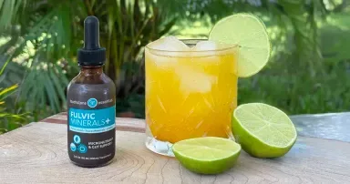 A glass of electrolyte mocktail with ice and citrus, set beside fresh oranges and lemons.