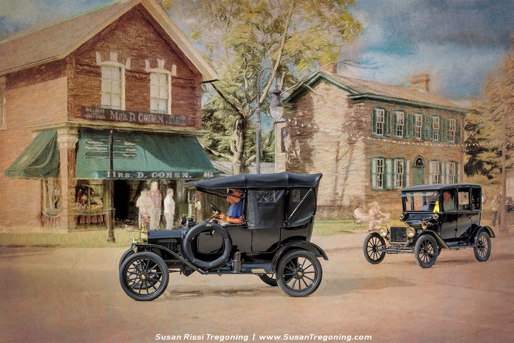 Two early Ford Model T automobiles travel down a village street lined with historic buildings. One car is an open‑top touring model and the other a closed‑top version, both rendered with a soft, painterly effect that emphasizes their rounded fenders, tall narrow wheels, and upright silhouettes. The storefront marked “Mrs. D. Cohen” with green awnings stands on one side of the street, while a brick house with green shutters anchors the other, creating the feel of an early‑20th‑century small‑town scene brought to life through digital illustration.