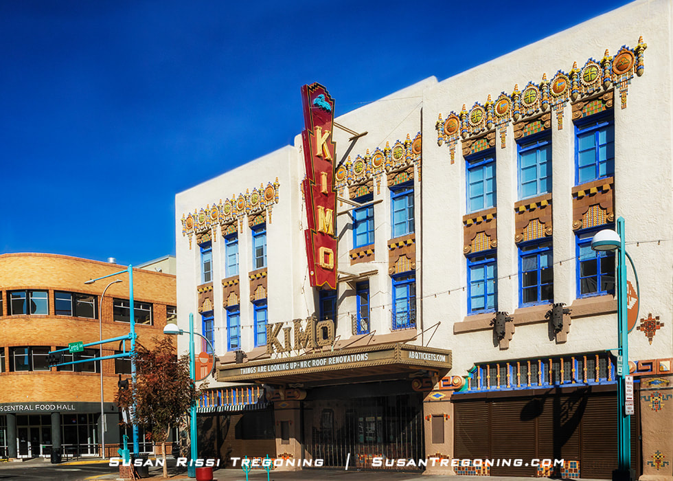 A historic theater building in Albuquerque, New Mexico, featuring Pueblo Deco architecture with colorful geometric patterns and blue‑framed windows. A tall vertical sign reads “KiMo,” and the marquee displays event information. A neighboring building labeled “Central Food Hall” is visible to the left.