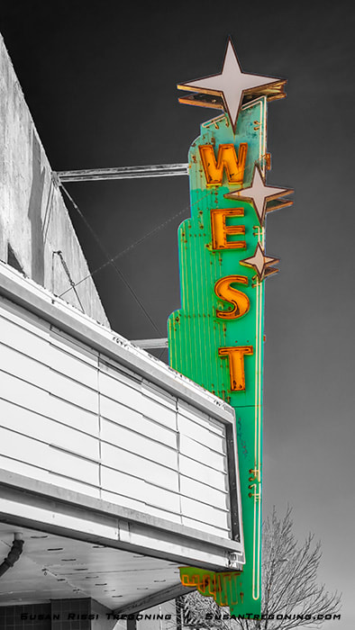 A vintage theater sign with a vertical green panel reading “West” in large orange letters outlined in neon. Three star shapes are attached near the letters. A white marquee sits below the sign, with part of the building façade and a dark sky visible in the background.