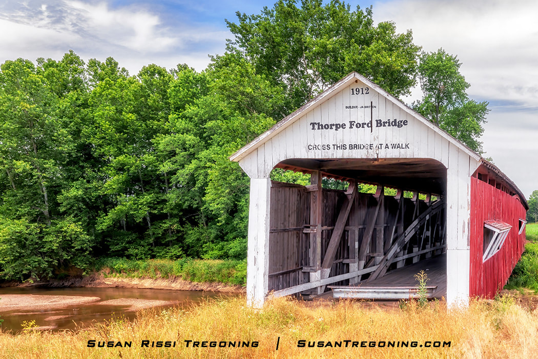 Thorpe Ford Covered Bridge, with a white entrance and red sides, spanning Big Raccoon Creek in Parke County, Indiana, surrounded by green trees and grass.