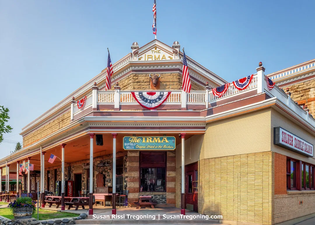 A view of the Historic Irma Hotel in Cody, Wyoming, showing its stone façade, upper balcony with patriotic bunting, and signage identifying it as Buffalo Bill’s original hotel.