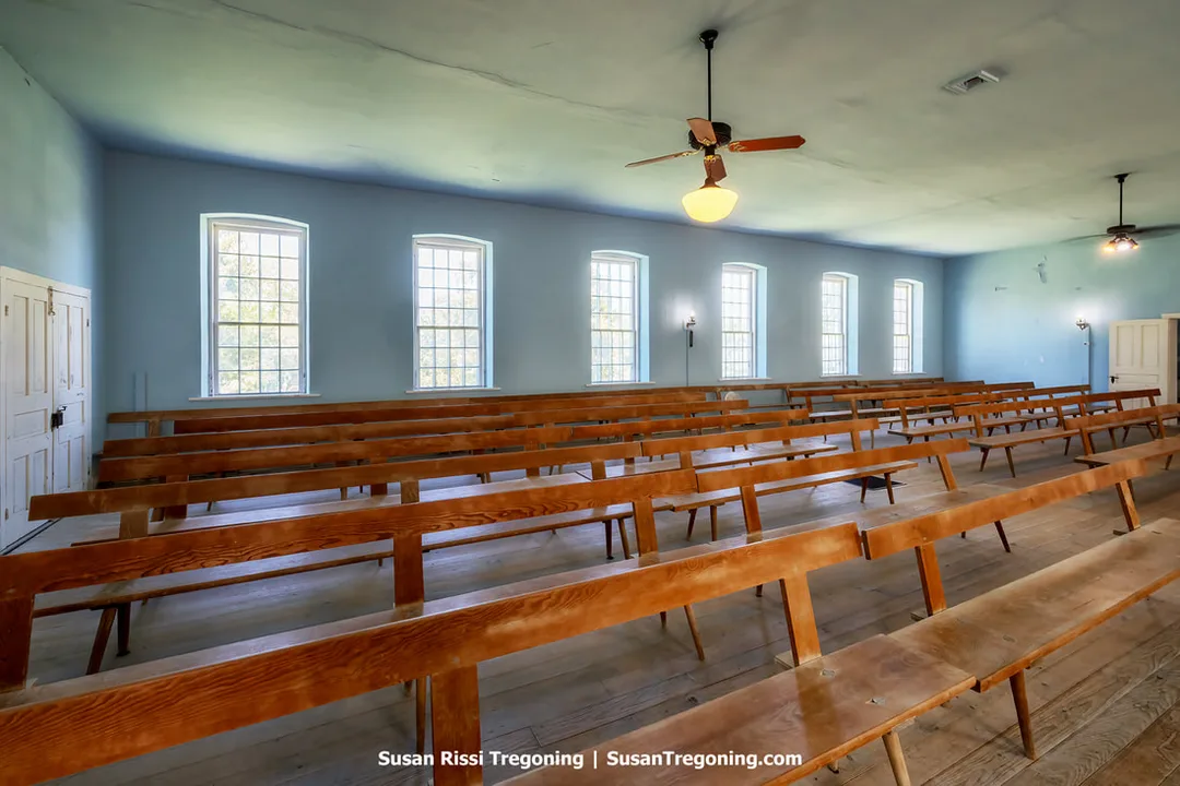 nside the Amana Community Church, with rows of plain wooden benches arranged in a long meeting‑hall layout. The interior features light blue walls and tall windows that reflect the simple, unadorned design of Inspirationist worship spaces.