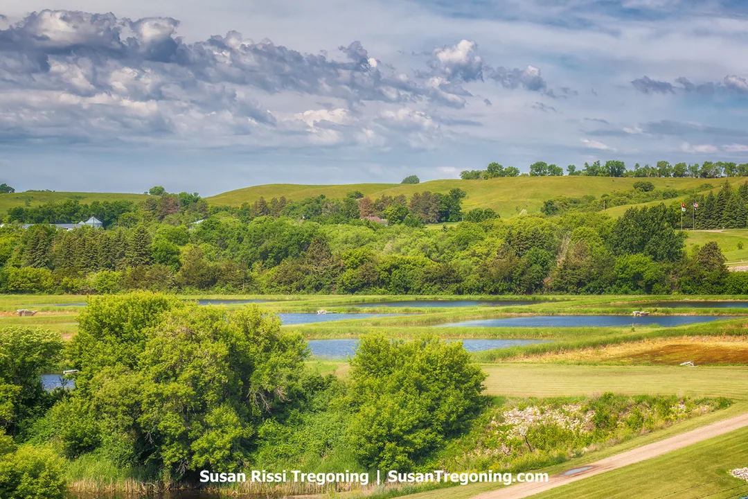View of green rolling hills and ponds near Lake Ashtabula in North Dakota. The ponds are part of the U.S. Army Corps of Engineers Water Management System within the Sheyenne River Valley landscape, surrounded by trees and open prairie under a partly cloudy sky.