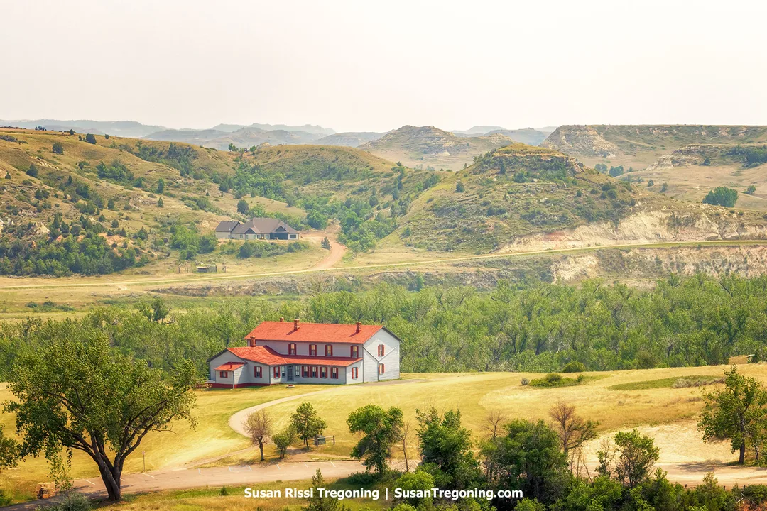 The historic Chateau de Mores, a two‑story mansion with red roofs and grey siding, stands on a hill overlooking the Badlands near Medora, North Dakota. Built in 1883 by the Marquis de Mores as a summer home for his family, the chateau is preserved as a state historic site and open for tours.