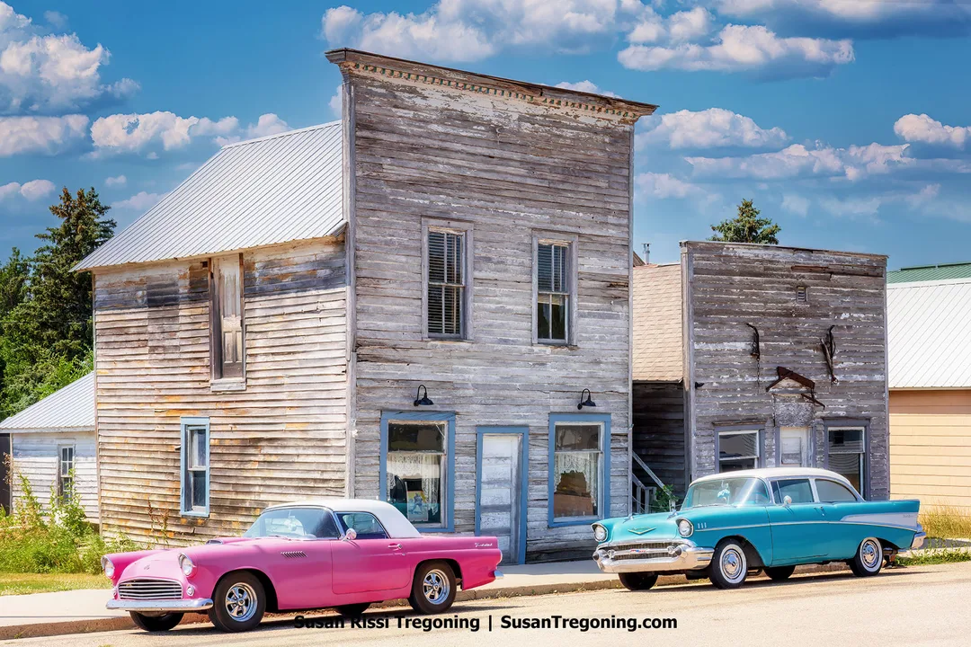 Early 1900s wooden storefronts in Kathryn, North Dakota, with a pink 1955 Ford Thunderbird and turquoise 1957 Chevrolet Bel Air parked in front, representing the town’s blend of prairie heritage and mid‑century Americana.