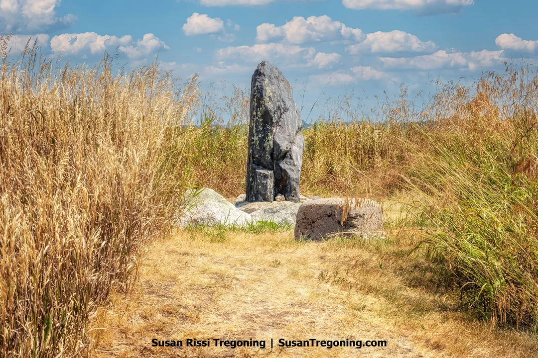tanding Rock monument at Standing Rock State Historic Site in North Dakota, viewed from a grass-lined path under a blue sky with scattered clouds.