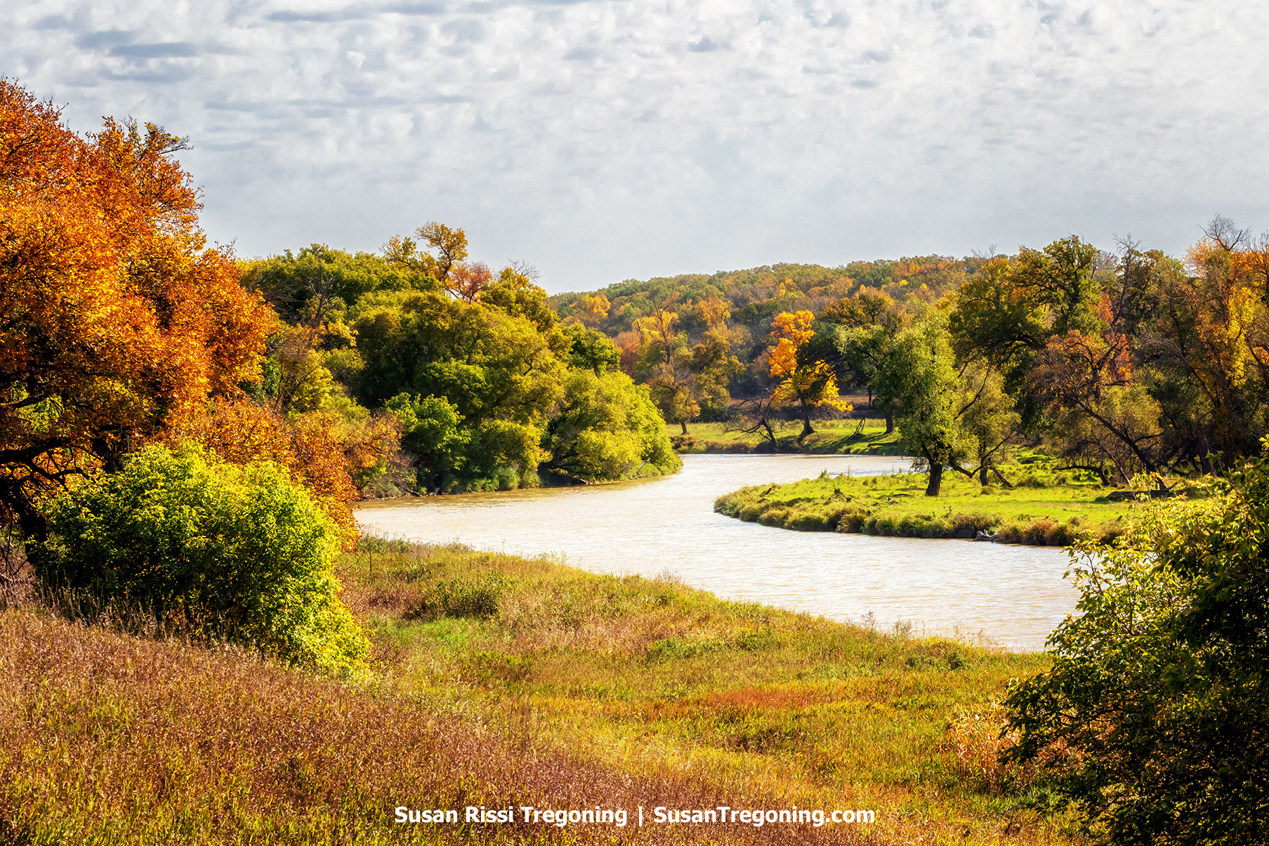 The Sheyenne River curves through a colorful autumn valley lined with trees, grasses, and wooded hills along the Sheyenne River Valley National Scenic Byway in North Dakota.
