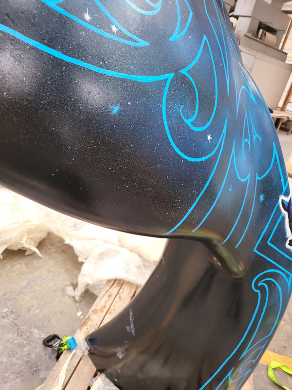 Close-up of blue painted artwork on the black “Kāpehu Whetū” whale-tail sculpture