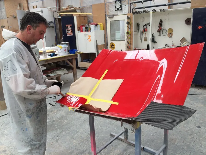 Worker applying carbon-fibre reinforcement to a red fibreglass mould