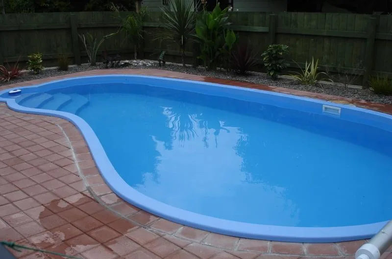 Freeform fibreglass swimming pool with a brick-paved surround