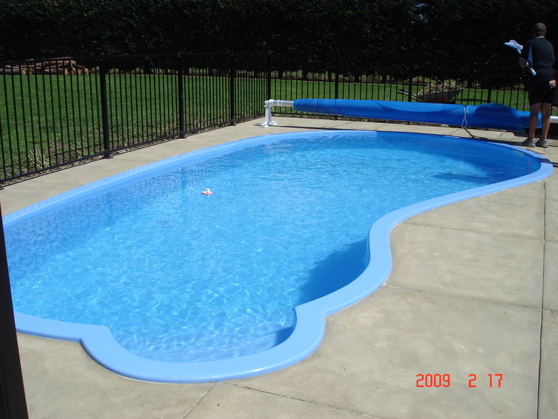 Freeform fibreglass swimming pool with a black safety fence