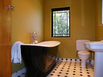 Black composite bath in a yellow bathroom with chequered floor tiles