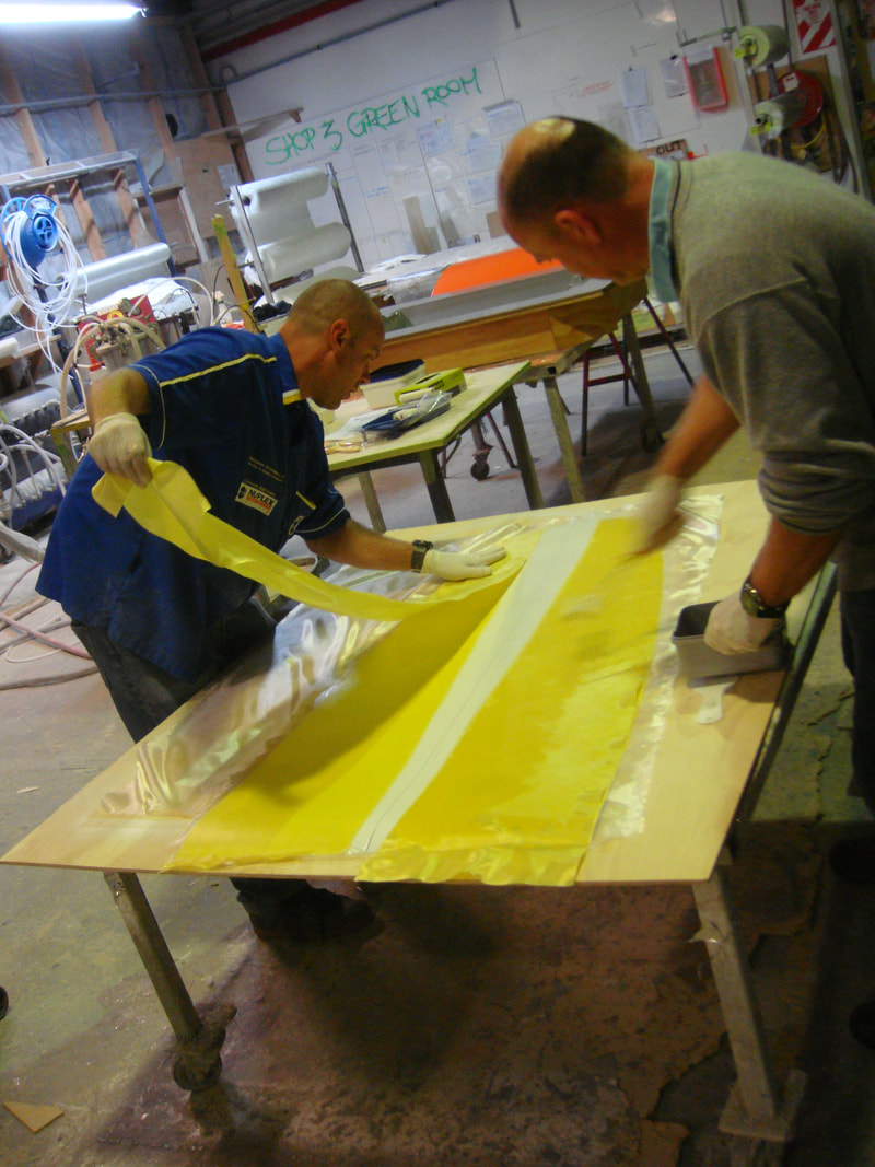 Workers hand-laminating a yellow fibreglass mould