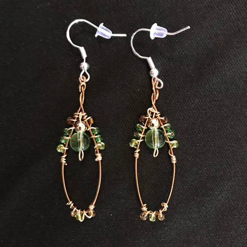 bronze wire shaped into oval earrings with green, brown, and gold beads
