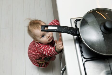 Young child reaching for a pan handle on a kitchen stove
