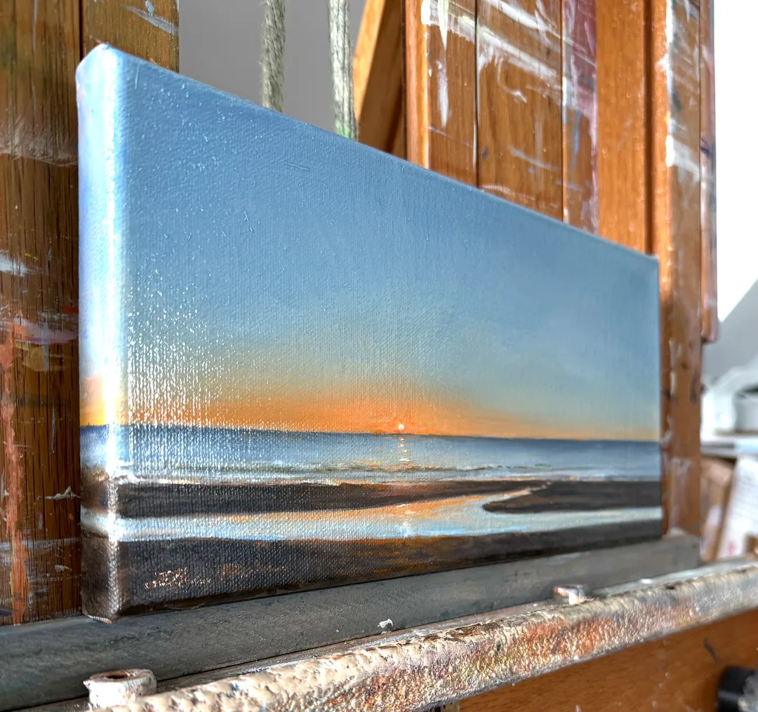 A radiant, small, oil painting of the sun rising over the Atlantic ocean, the sky gradually going from blazing on the horizon to deep blues, all reflected in a tidal pool in the foreground sand.