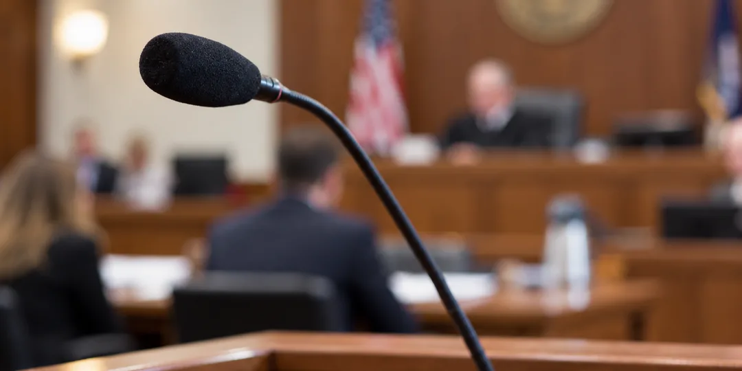 Close up image of gooseneck microphone shown in focus with courtroom out of focus in background.