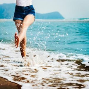 Image of person skipping along shoreline of ocean, kicking feet through the waves.