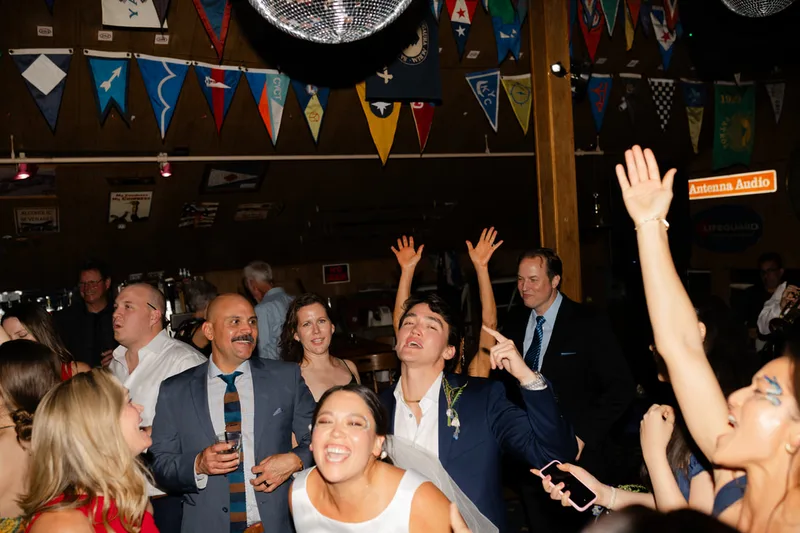 A group of smiling adults singing and dancing at a wedding in Sausalito, California. The group is sporting fun glitter and face paint from the Glitter Bar.