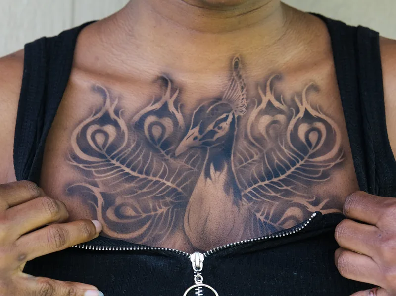 a dark skinned person in Oakland, California, is modeling a realistic airbrush tattoo on their chest of a peacock with a fanned tail