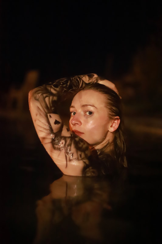 a young white woman with blonde hair modeling two full sleeves of waterproof airbrush tattoo's while half submerged in a pool in Marin, California