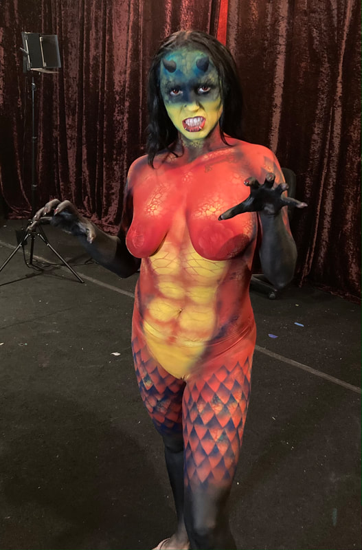 Woman body painted into a yellow and red dragon in Oakland, Ca. She is covered in scales and has prosthetic horns on her head