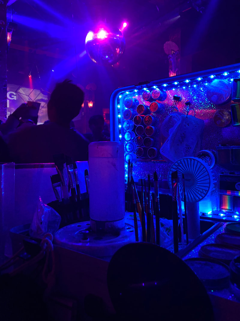 A dark night club is lit up by LED lights from a face painting kit