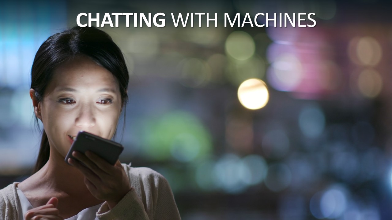 A woman with dark hair tied back, her face lit by the glow of her phone, speaks into the handset held close to her mouth and smiles slightly. Behind her, city lights blur into soft coloured circles at night. Headline across the top reads “Chatting with machines”, with “Chatting” in bold.