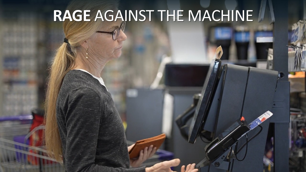 A woman with a long blonde ponytail and glasses, seen in profile at a supermarket self-checkout, holds a tan leather wallet and gestures at the screen with an open palm, her expression wary and weary. Headline text across the top reads “Rage against the machine”, with “Rage” in bold.