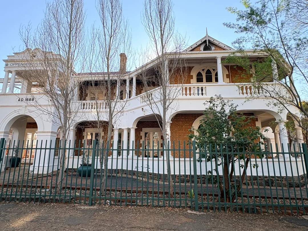 Oppenheimer House, formerly Nazareth House, viewed from Cornwall Road in Kimberley, showing its 1888 date, red-brick walls, white verandas, arches and columns.