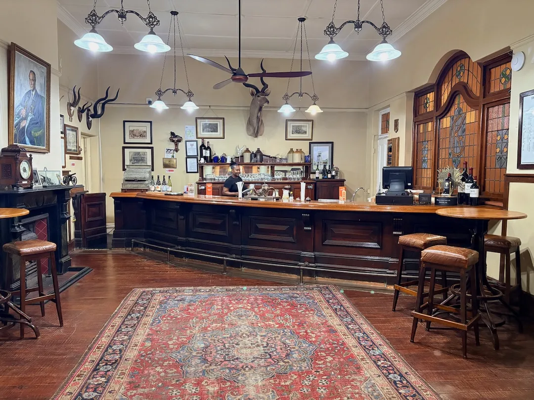 Historic timber bar at the Kimberley Club, with polished wood counter, high stools, stained-glass windows and traditional club furnishings.