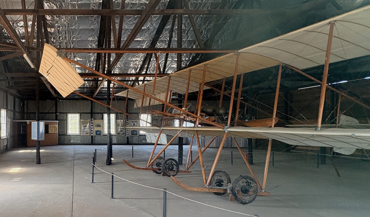 Side view of the replica Compton Paterson biplane showing its wooden frame, fabric-covered wings and large wooden propeller mounted behind the pilot’s seat between the upper and lower wings.