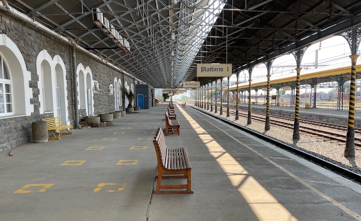 View along Platform 1 at Kimberley Railway Station showing the historic canopy, station signs, benches and railway tracks.