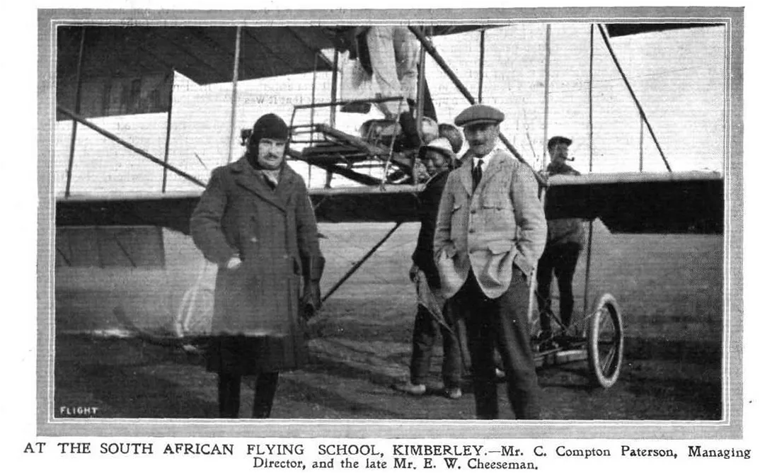 Historic photograph of C. Compton Paterson and E. W. Cheeseman standing beside an early biplane at the South African Flying School in Kimberley.