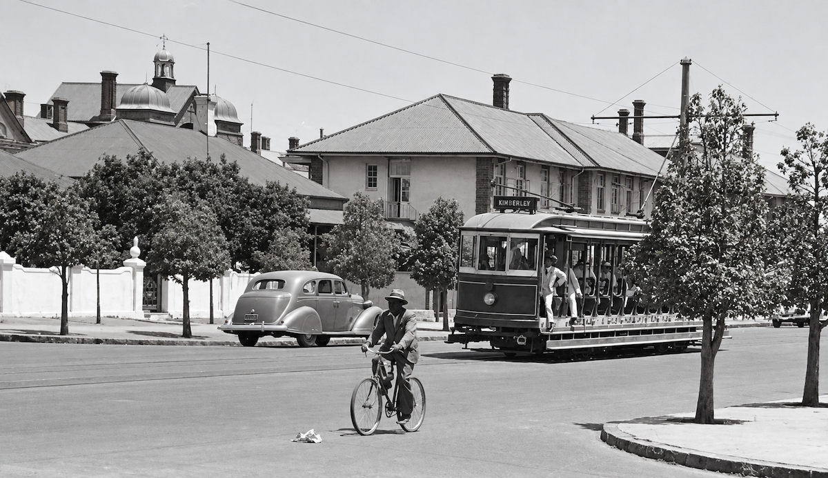 1930s street scene on Du Toitspan Road, Kimberley, showing a tram to Beaconsfield approaching Memorial Road, with the Grewer Memorial Nurses’ Home in the background and the old Kimberley Hospital building behind it.