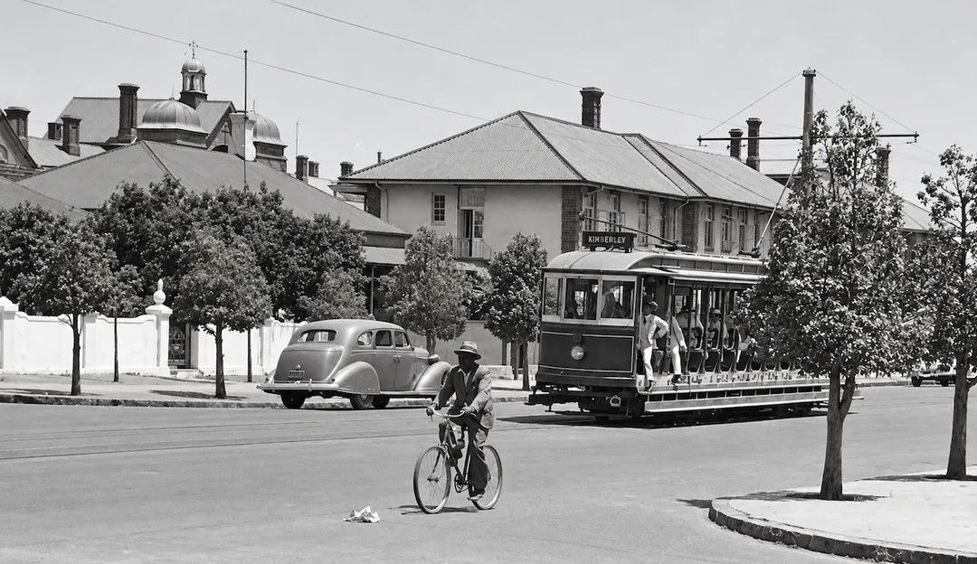 1930s street scene on Du Toitspan Road, Kimberley, showing a tram to Beaconsfield approaching Memorial Road, with the Grewer Memorial Nurses’ Home in the background and the old Kimberley Hospital building behind it.