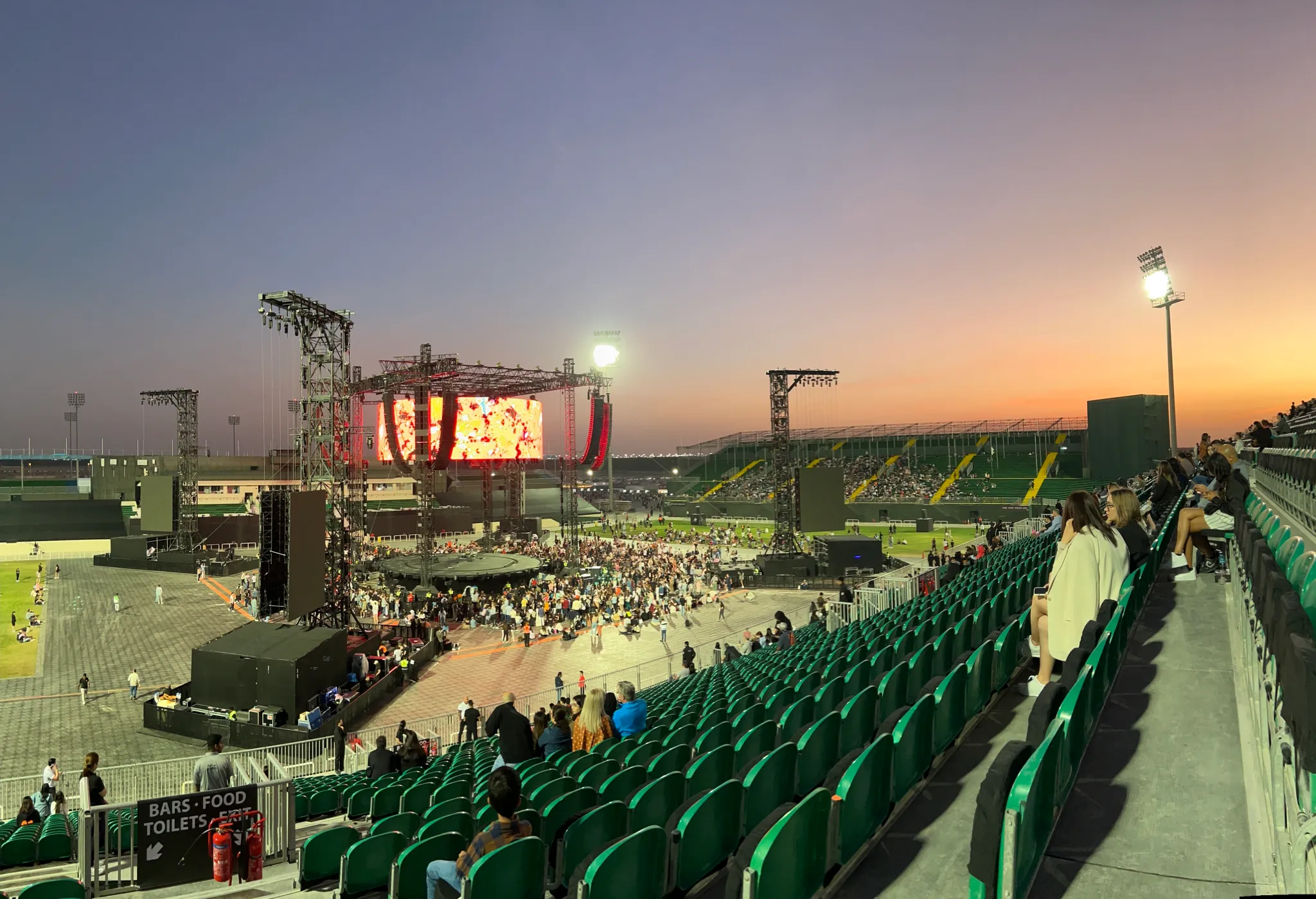 Wide view of Ed Sheeran's concert at Dubai Sevens ground, showing the stage, audience and stadium seating at sunset.