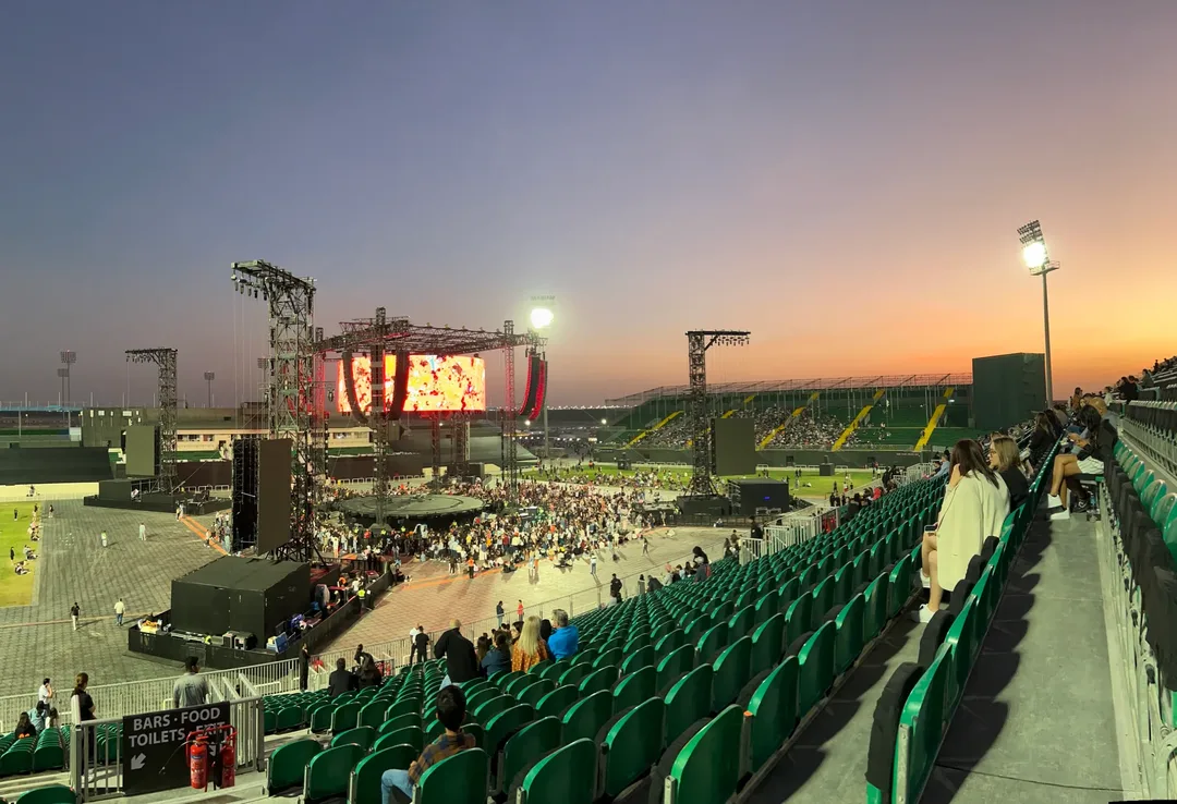 Wide view of Ed Sheeran's concert at Dubai Sevens ground, showing the stage, audience and stadium seating at sunset.