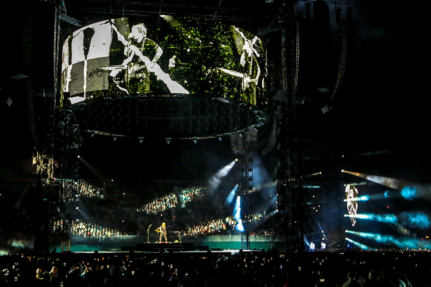 Large-scale Ed Sheeran concert with a central stage, suspended video screens, lighting and a packed audience in Dubai.