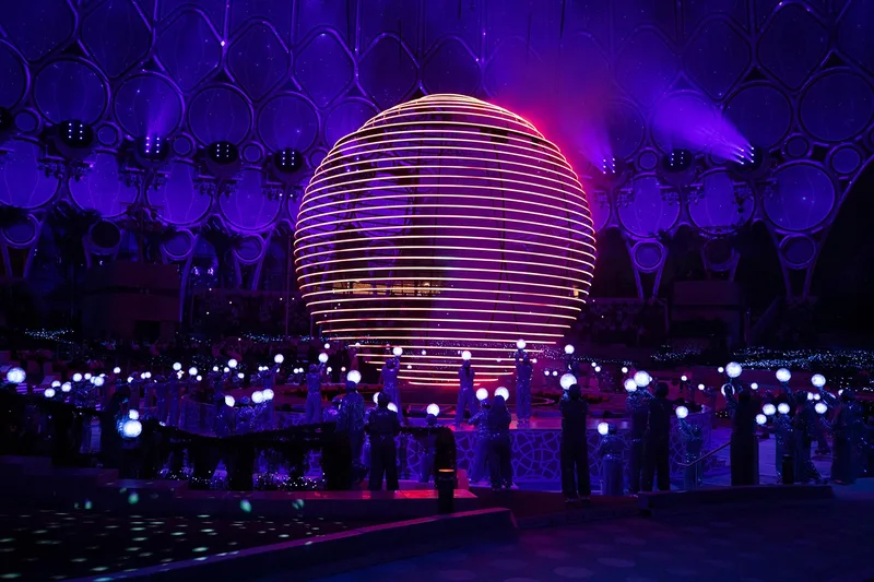 Large illuminated spherical scenic feature at a nighttime event with guests gathered around it.