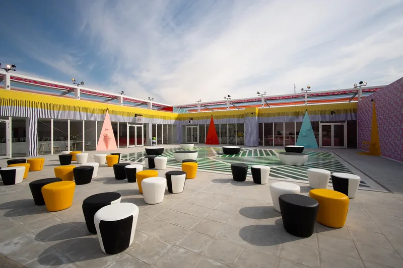 Outdoor courtyard with colourful event furniture, shaded structures and temporary hospitality setup.